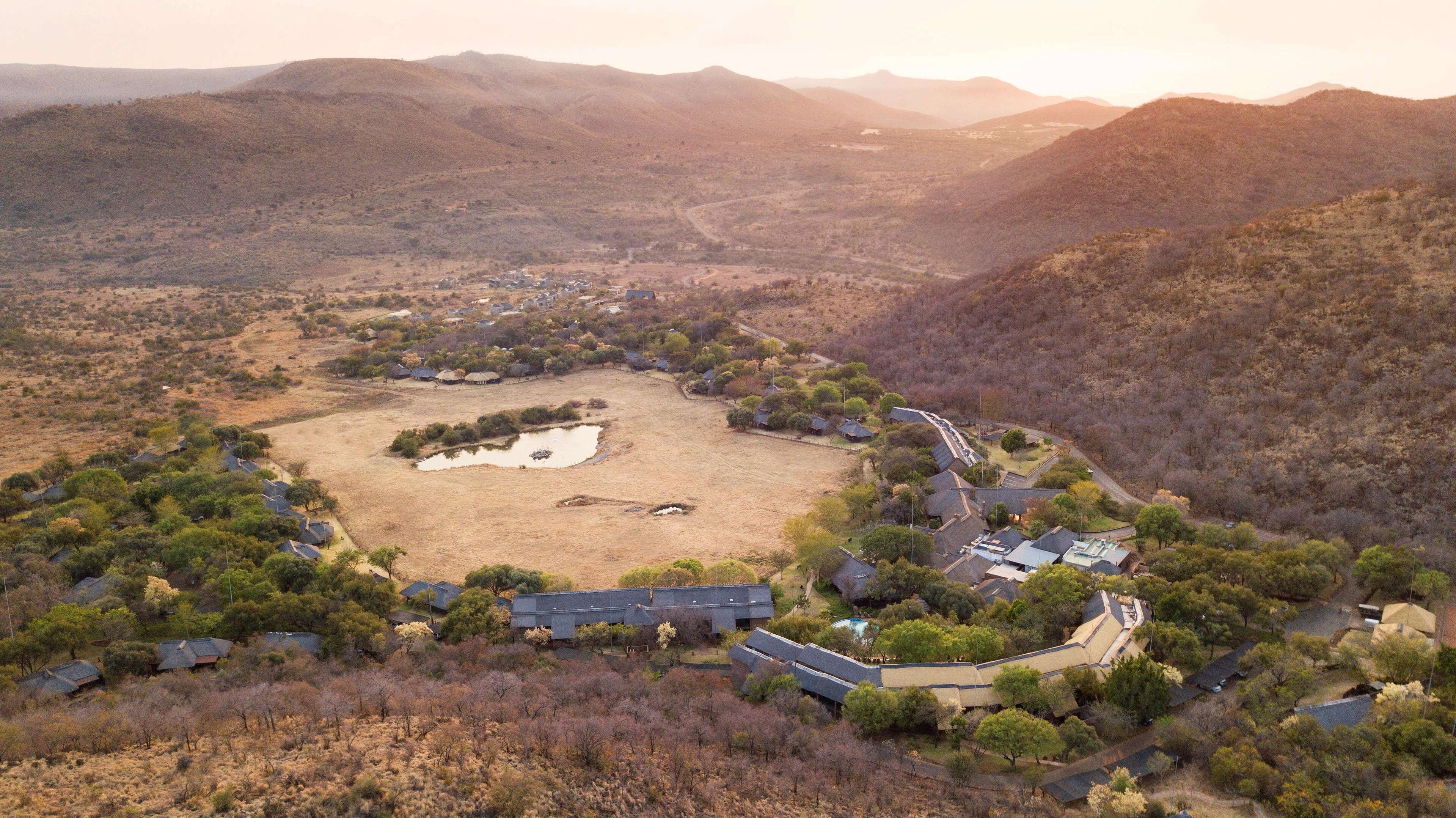 An aerial view of a residential area with houses, a central open space, and surrounding hills.