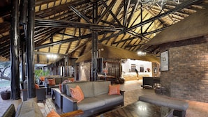 A spacious lounge area with high ceilings, exposed beams, and a thatched roof. - Bakubung Bush Lodge (Pilanesberg National Park)