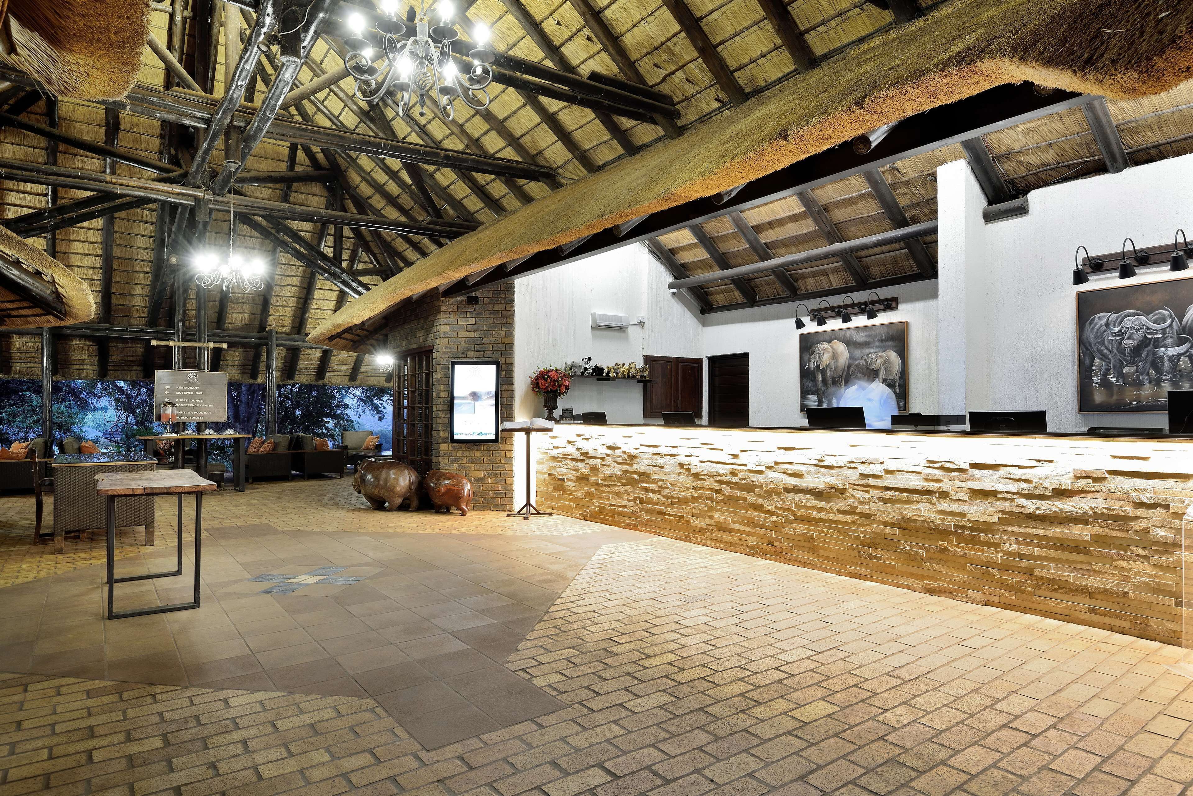 An interior with a high ceiling, exposed beams, a brick wall, and a tiled floor.