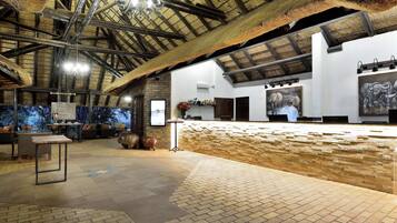 An interior with a high ceiling, exposed beams, a brick wall, and a tiled floor.