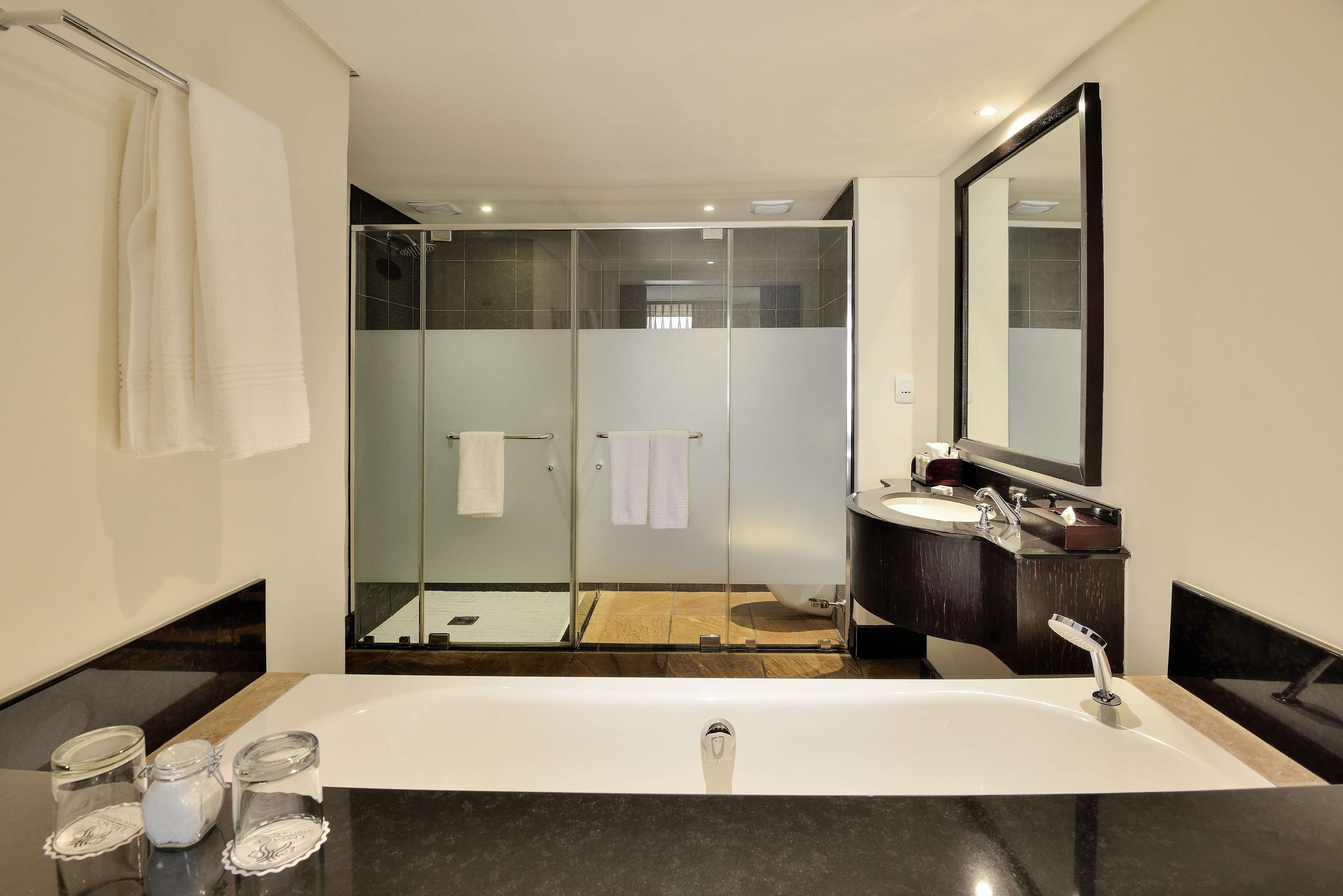 A modern bathroom with a large bathtub, a glass-enclosed shower, and a dark wooden vanity with a mirror.