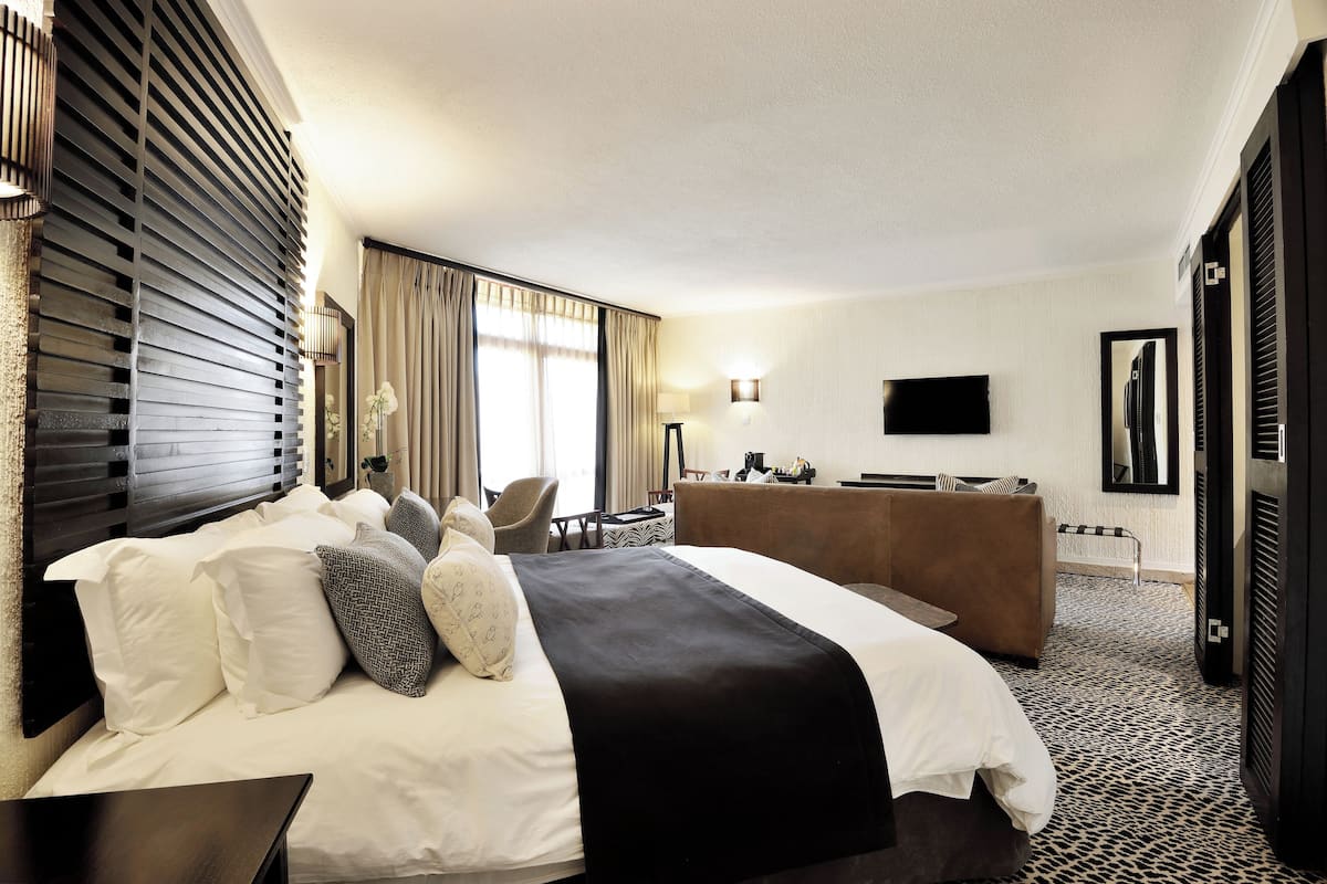 Una habitación de hotel con una cama grande, un escritorio, una silla, un televisor y una ventana con cortinas.