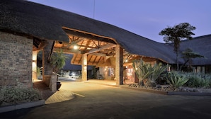 A building with a thatched roof and brick walls, a paved entrance, and surrounding greenery. - Bakubung Bush Lodge (Pilanesberg National Park)
