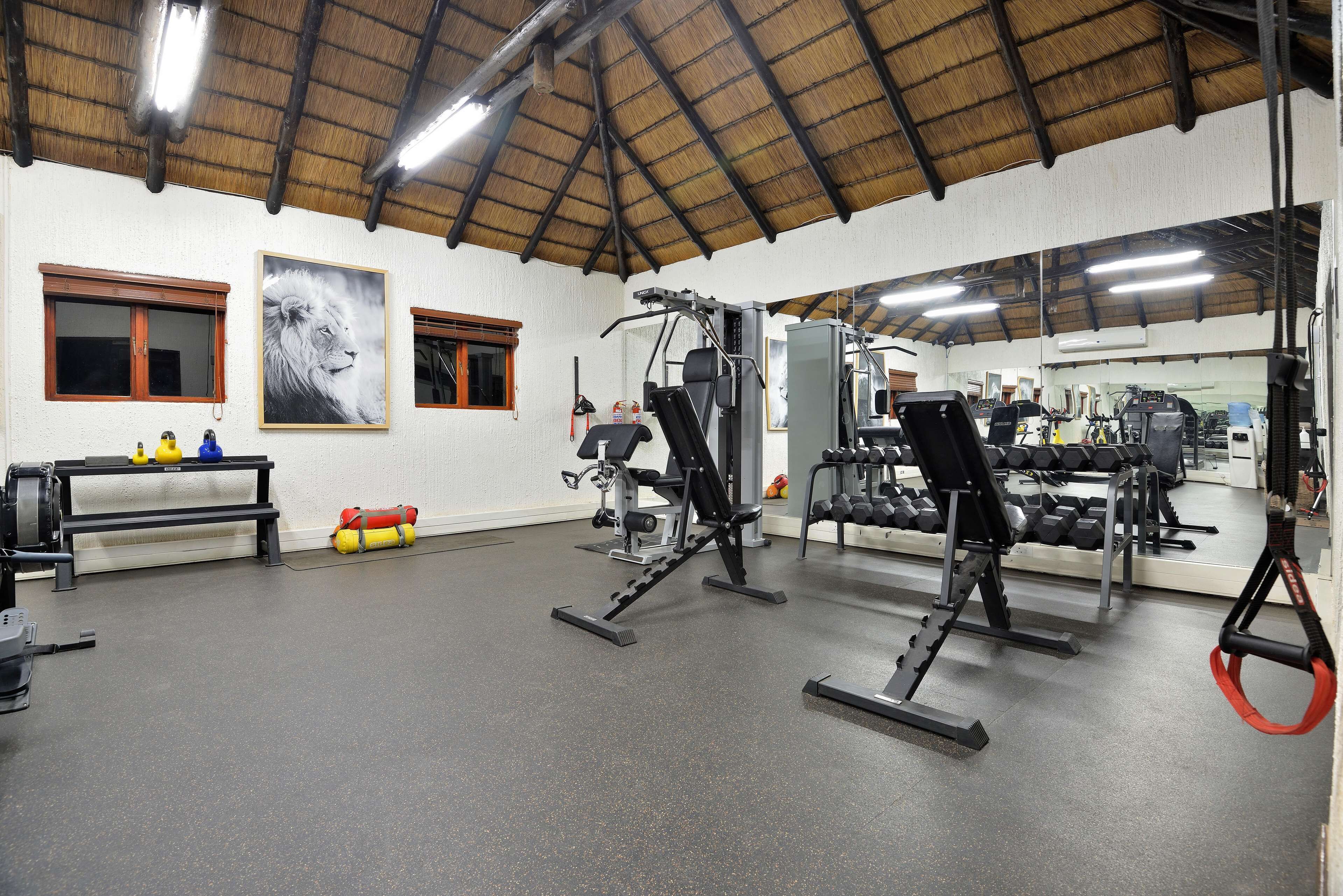 Une salle de sport équipée de divers appareils d’exercice, dotée d’un grand miroir et d’un plafond avec des poutres apparentes.