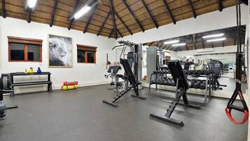 Ein Fitnessraum mit unterschiedlichen Trainingsgeräten, einem großen Spiegel und einer Decke mit freiliegenden Balken.