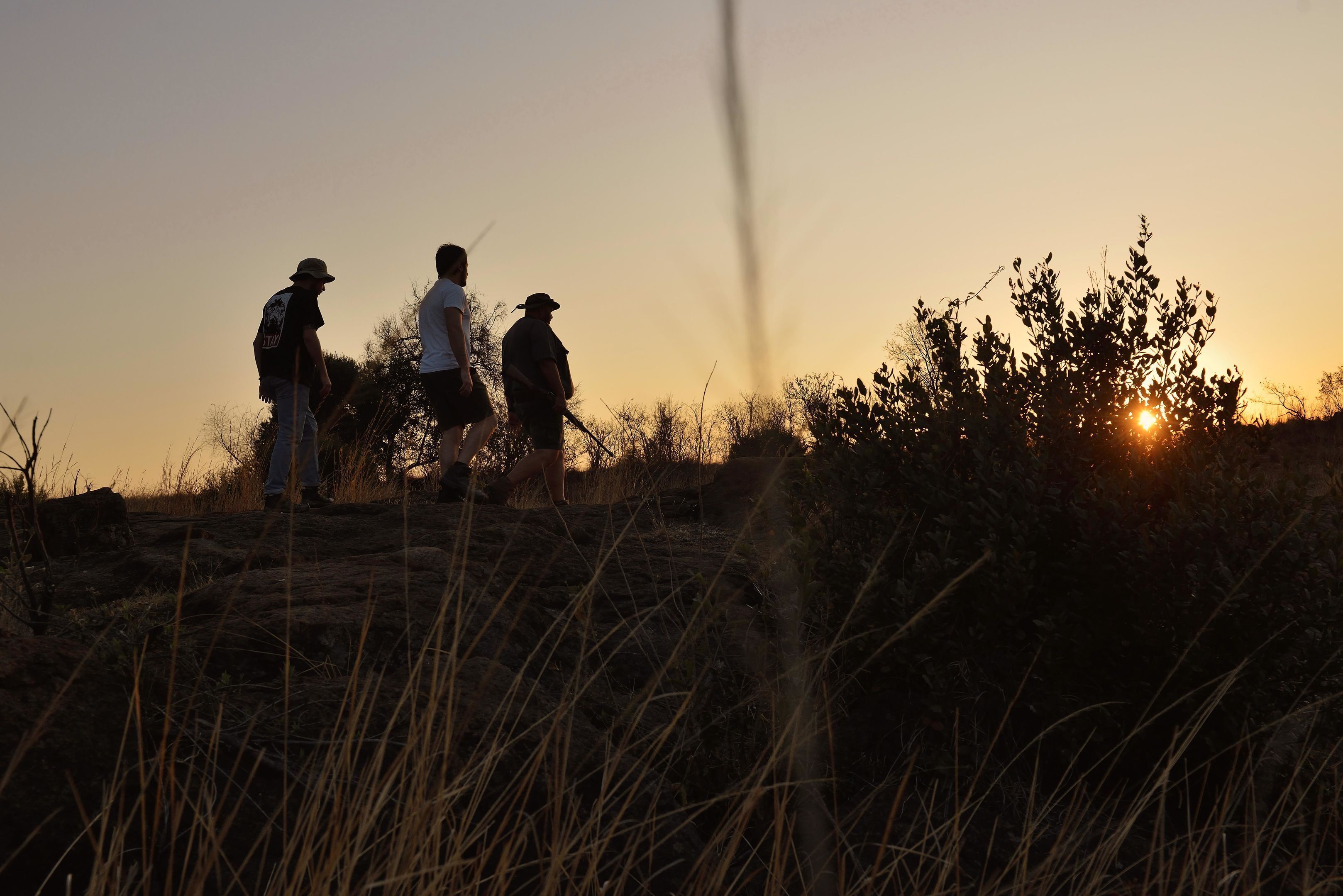 Three people standing on a grassy hill during sunset.