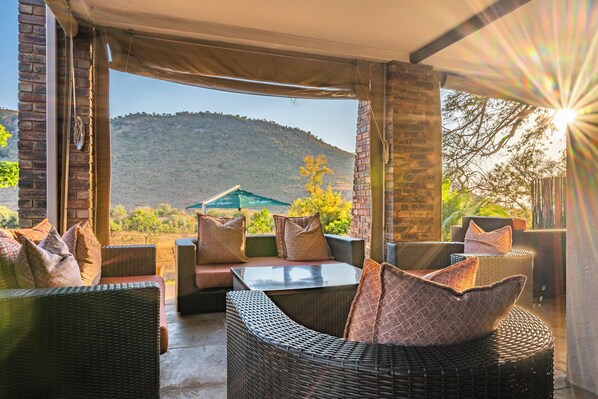 Un patio al aire libre con mobiliario de mimbre, una mesa de vidrio y vistas a un paisaje montañoso.