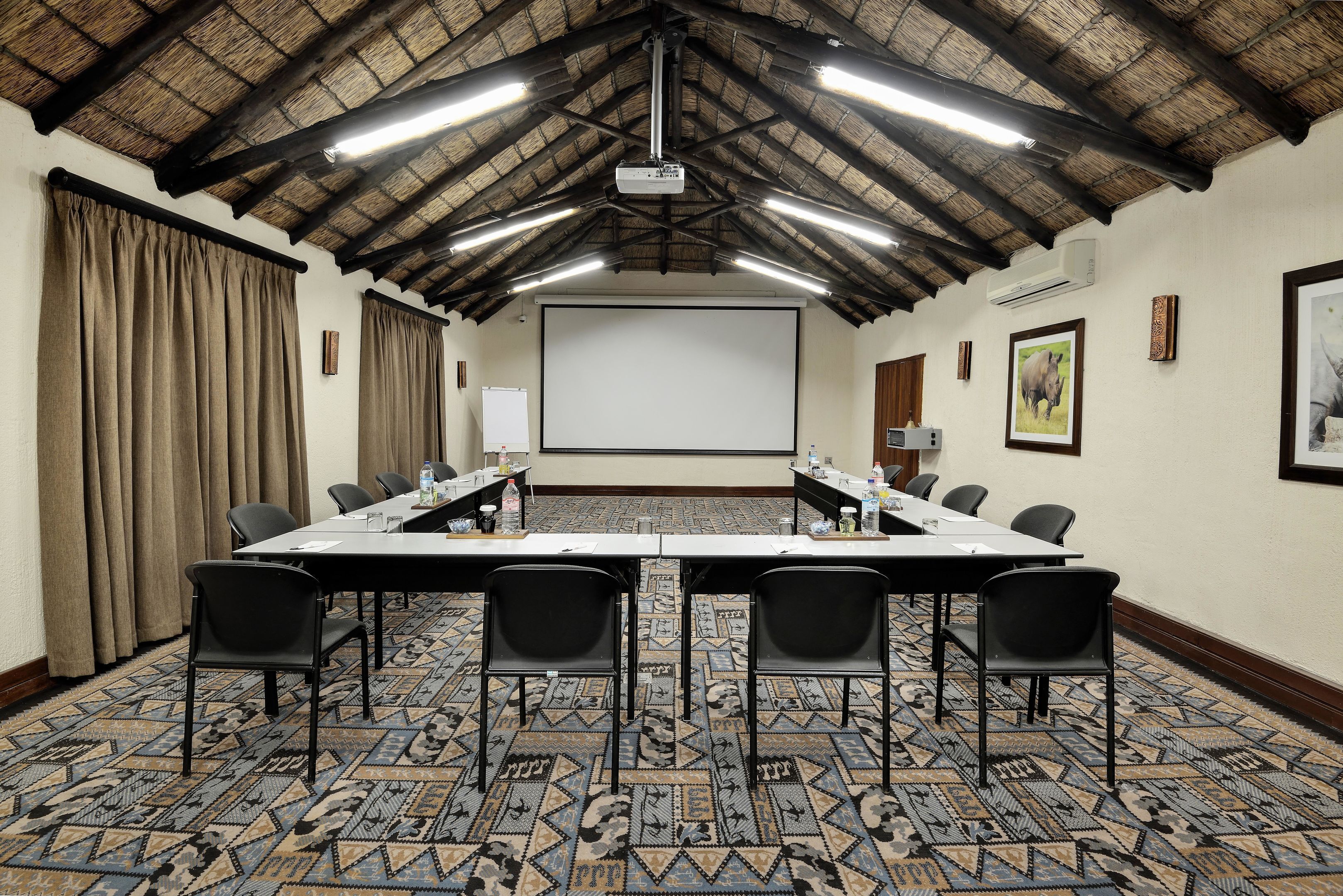 Un salón de conferencias con una larga mesa, sillas, un proyector y una pantalla.