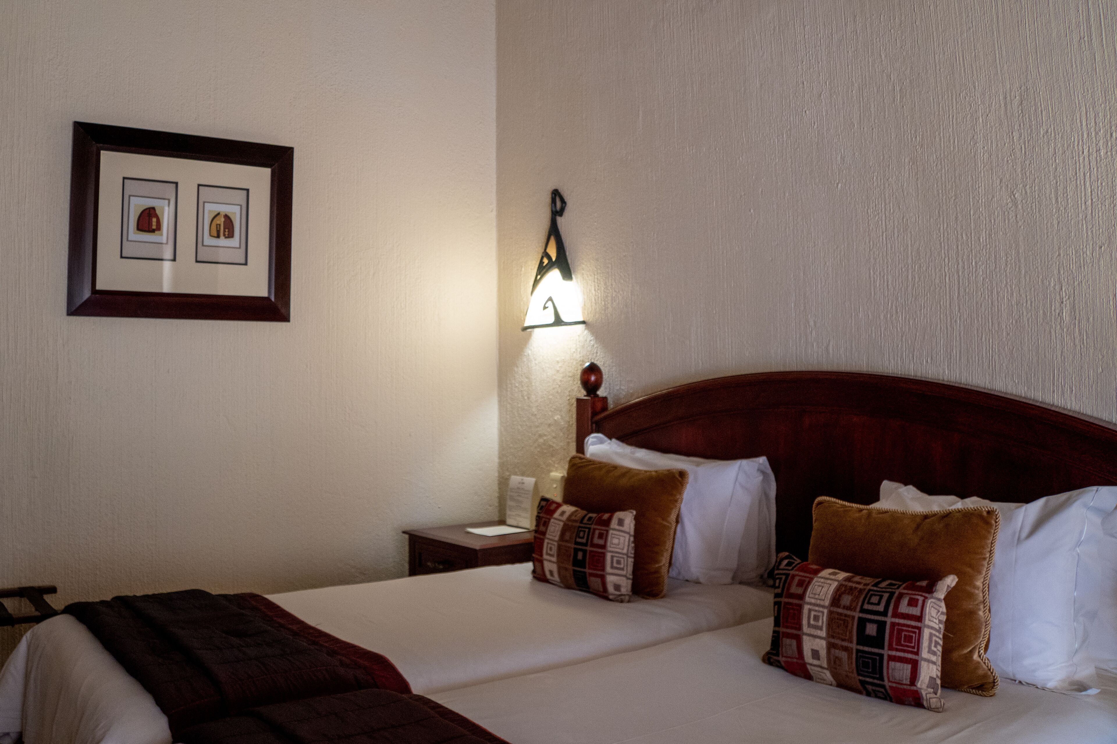 A hotel room with a large bed, two pillows, a nightstand, a framed picture, and a wall-mounted light fixture.
