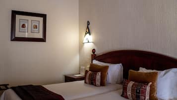A hotel room with a large bed, two pillows, a nightstand, a framed picture, and a wall-mounted light fixture.