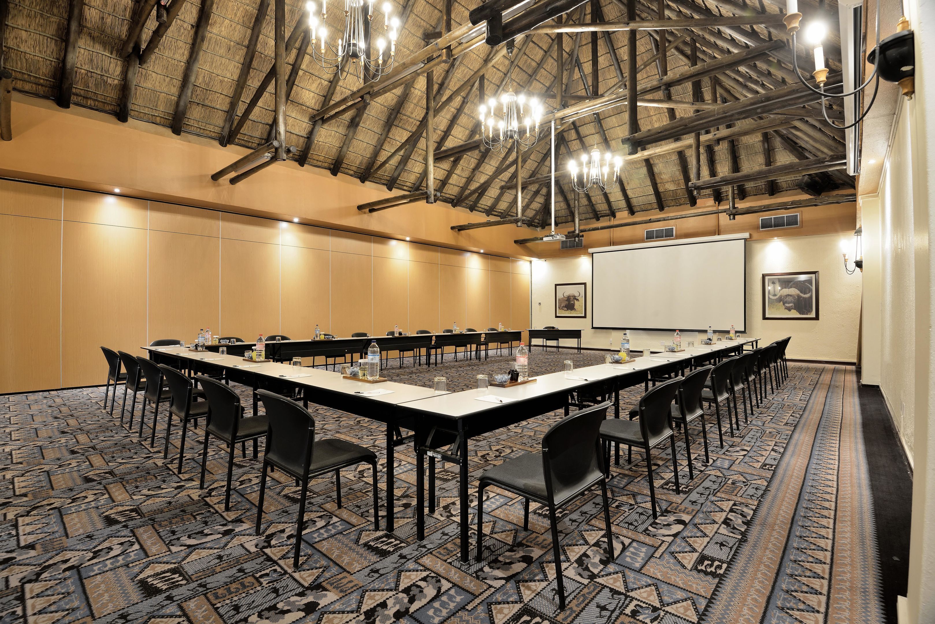A conference room with a long table, black chairs, a projector screen, and a patterned carpet.