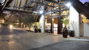 L’entrée d’un hôtel, avec un passage couvert, des plantes en pot et une façade bien éclairée.