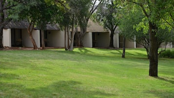 A courtyard with a lawn and several trees. There are buildings with thatched roofs in the background.