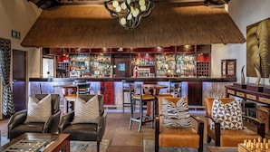 A bar area with leather seating, a thatched ceiling, and a variety of bottles on shelves.