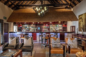 Uma área de bar com assentos de couro, teto de palha e uma variedade de garrafas em prateleiras.