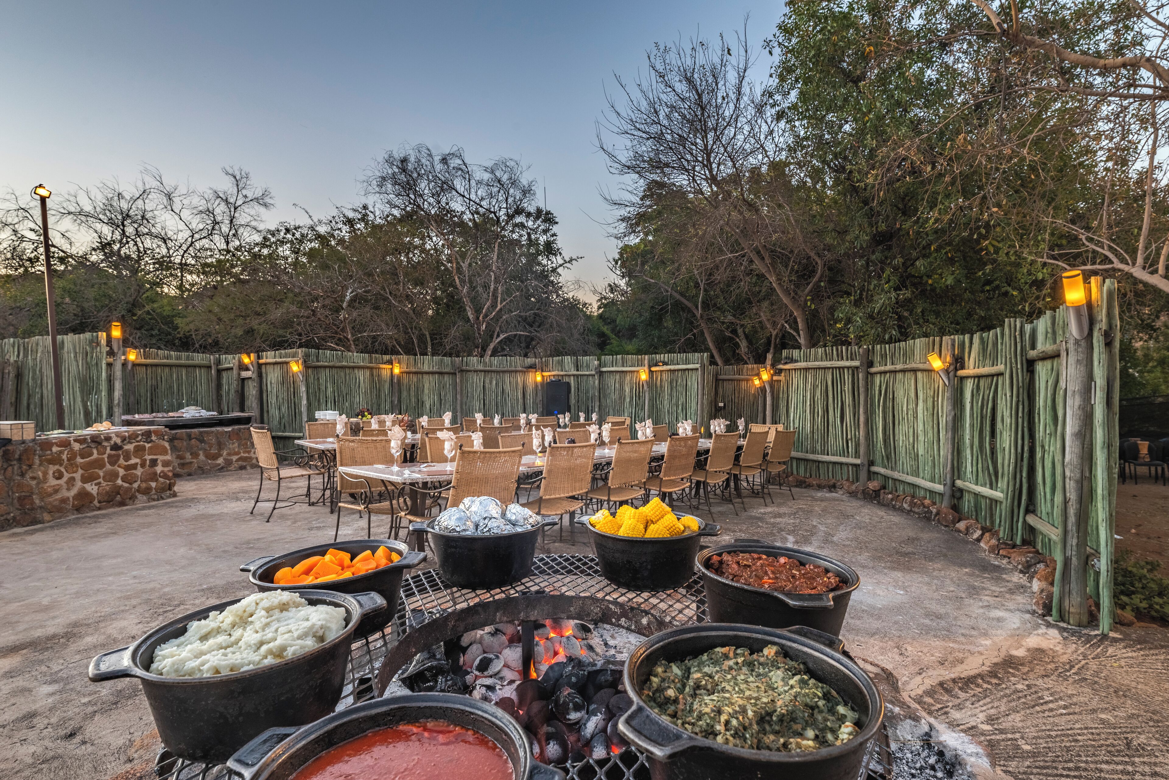 Un espace de restauration en plein air, avec des tables et des chaises, entouré d ’une clôture en bois, et divers aliments présentés dans des récipients.