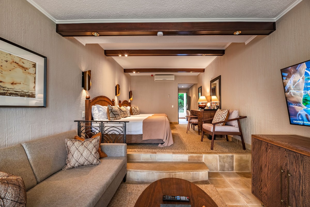 A hotel room with a bed, a sofa, a coffee table, a TV, and a desk with a chair.