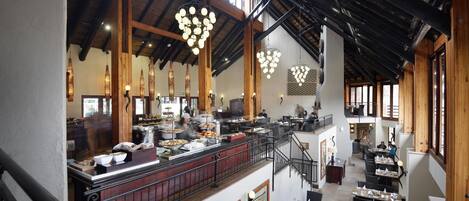 Un restaurant spacieux avec de hauts plafonds, des poutres en bois et des luminaires suspendus.