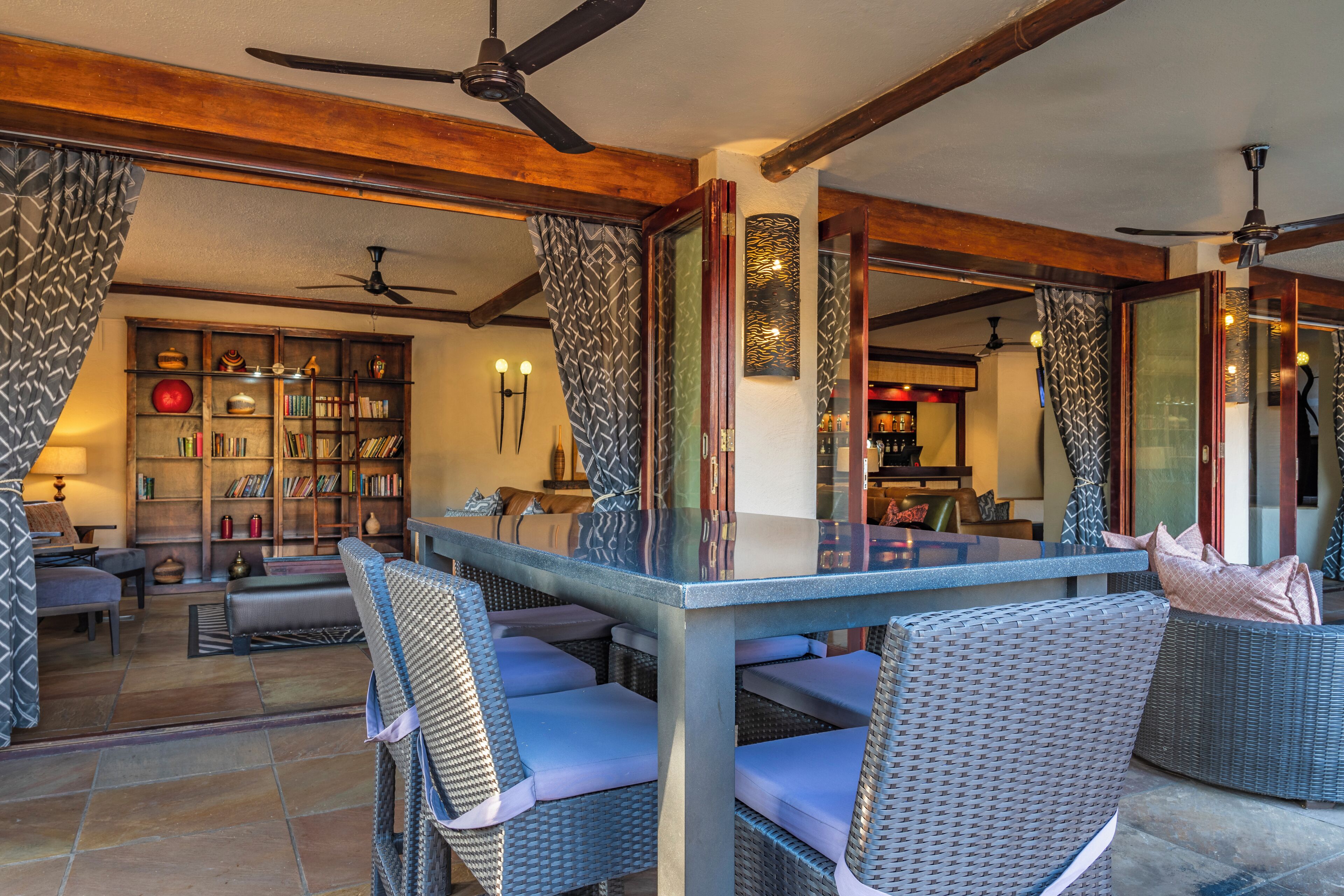 A spacious living area with a glass-top table, wicker furniture, and a bookshelf filled with books.