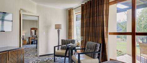 A hotel room with a bed, a seating area with a table, a television, and a view of the outdoors.