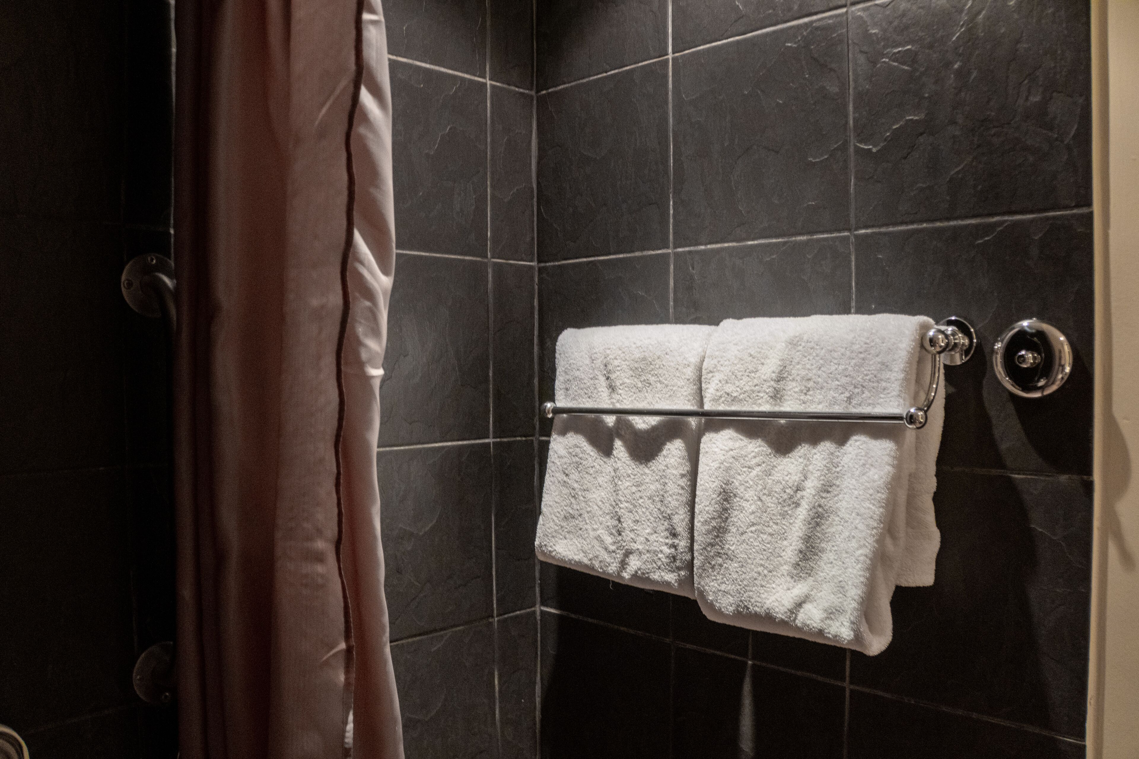 A bathroom with dark tiled walls, a towel rack with two white towels, and a shower curtain.