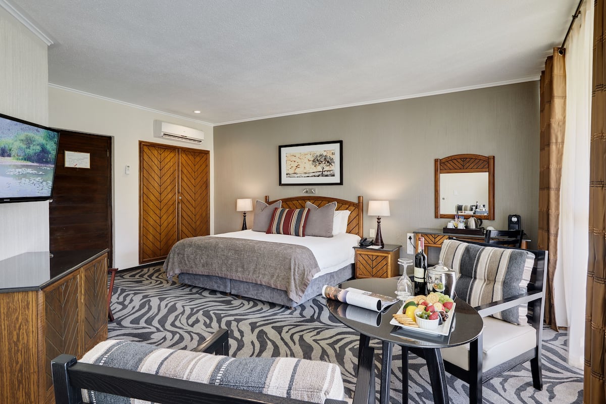 A hotel room with a bed, a TV, a desk with a chair, and a dining table with a fruit platter.
