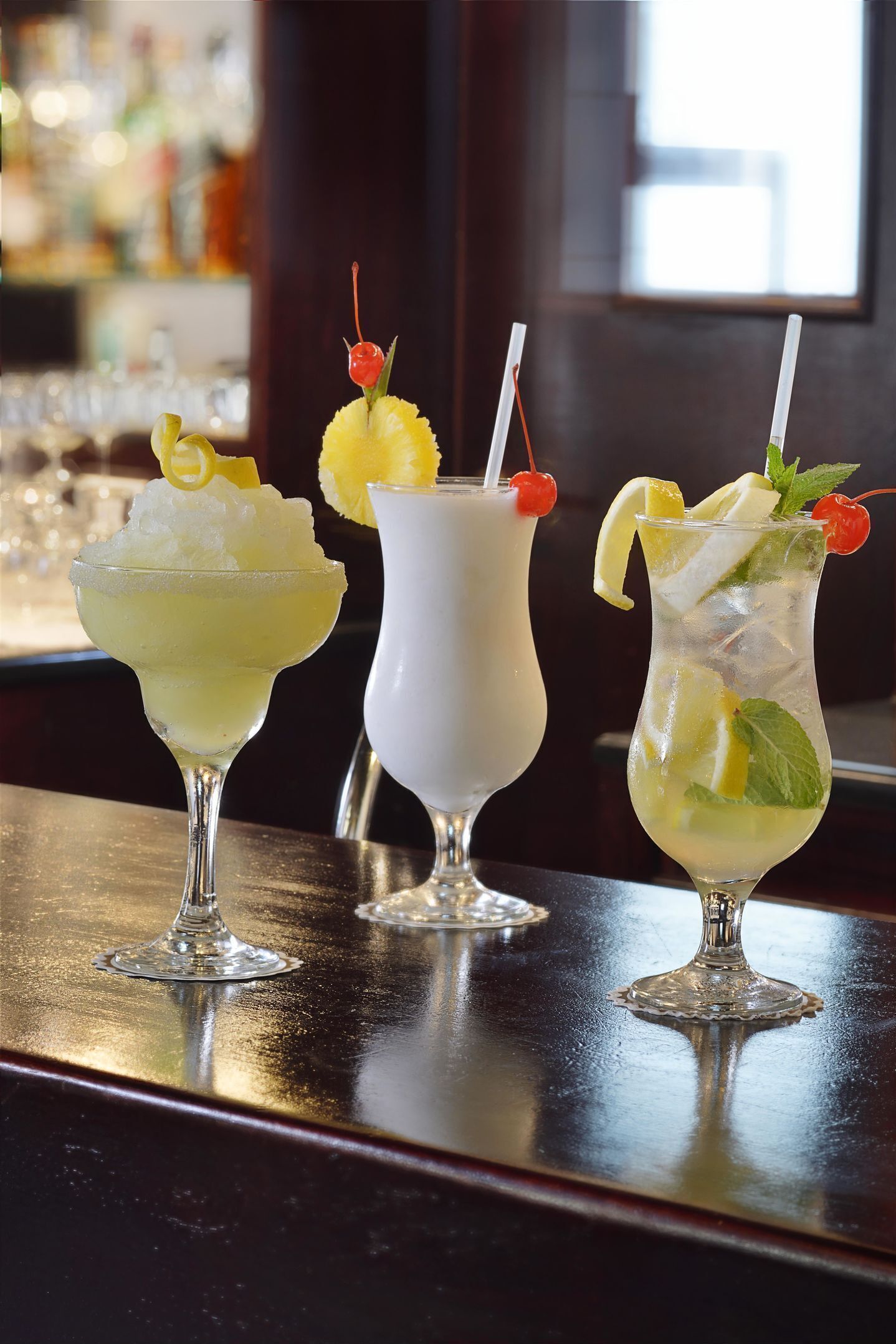 Three cocktails on a bar counter with a blurred background of bottles.