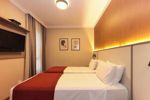 Una habitación de hotel con dos camas, un televisor montado en la pared y obras de arte decorando la pared.