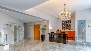 A modern lobby with marble flooring, a reception desk, a chandelier, and a clock on the wall. - H4 Hotel Opera Jardins (São Paulo)