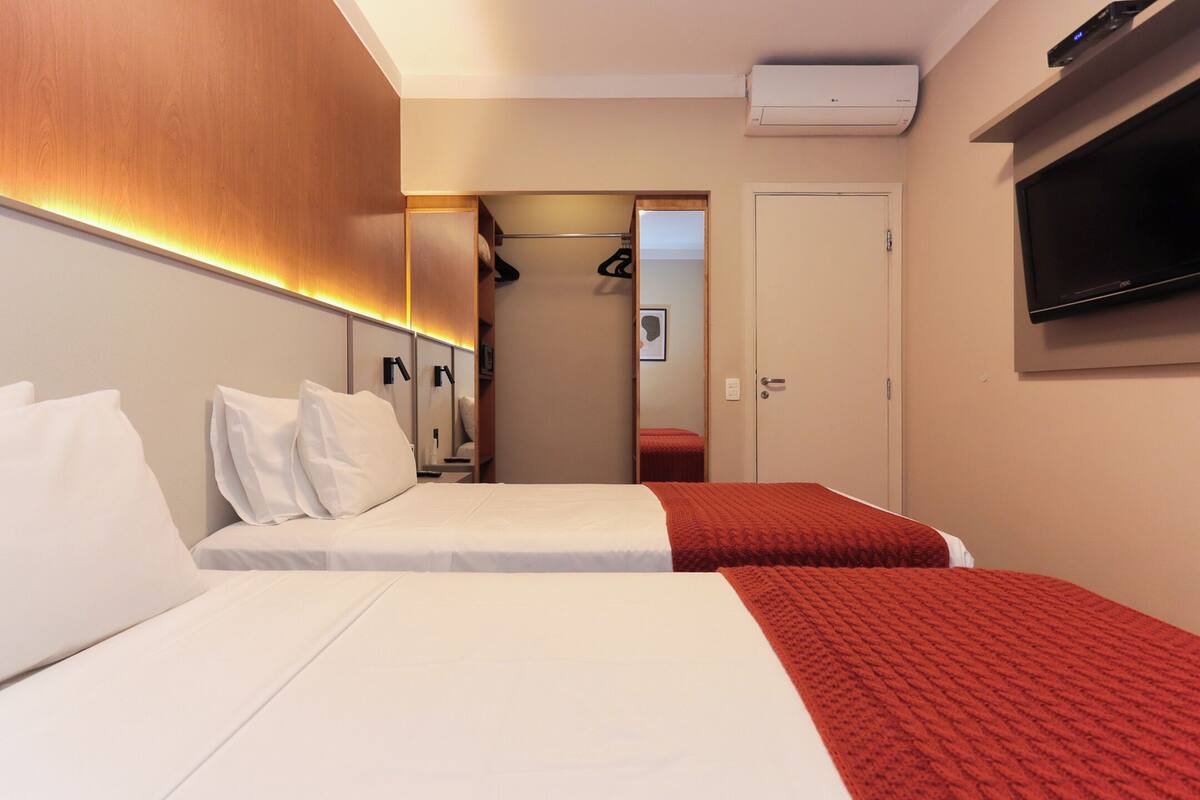 Habitación de hotel con dos camas, televisión, armario y espejo.