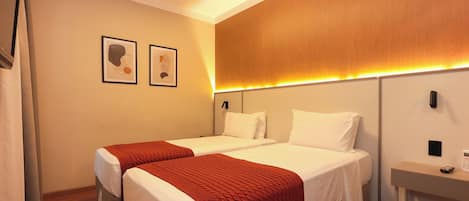 Habitación de hotel con dos camas, cabecera de madera, mesita de noche con teléfono y dos cuadros en la pared.