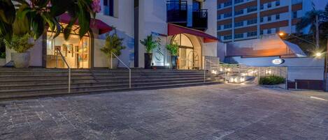 A hotel entrance with a modern design, featuring a staircase leading to the entrance, a red awning, and a signboard.