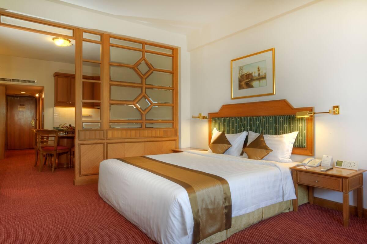 Habitación de hotel con una cama grande, cabecera de madera, escritorio con teléfono y zona de comedor con una silla y mesa.