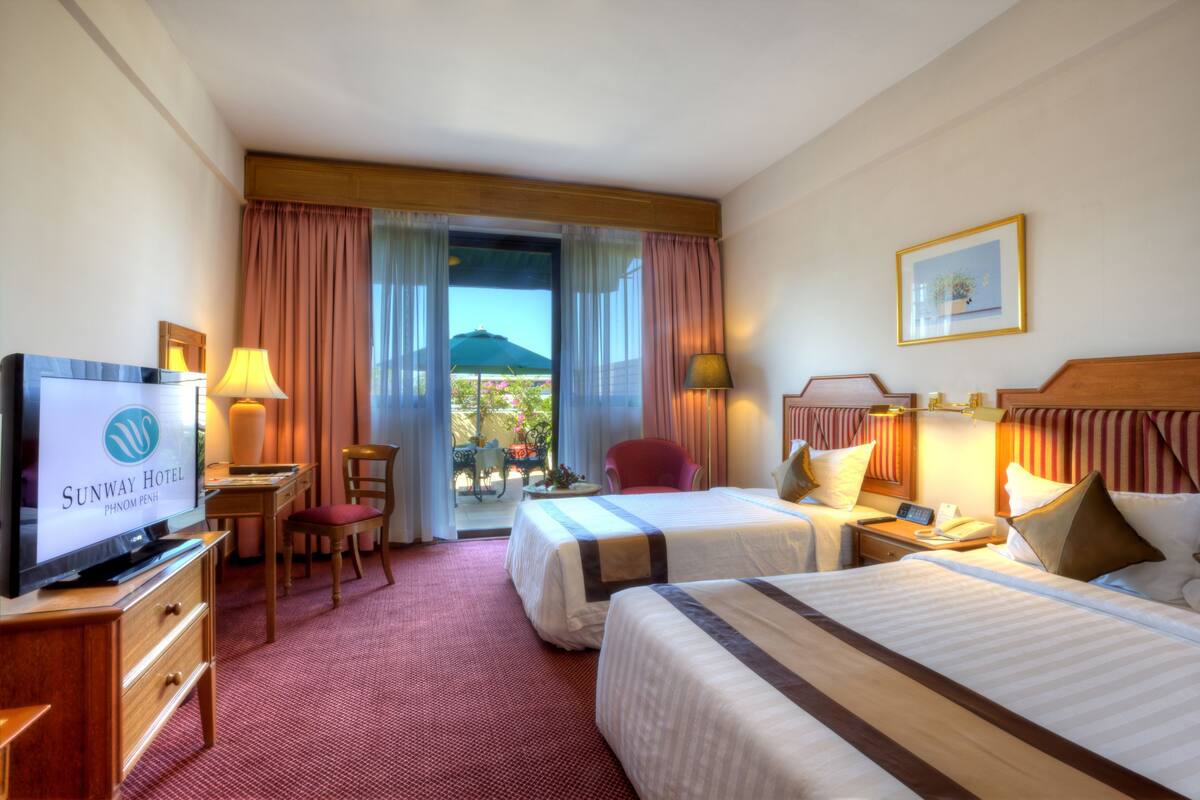 Habitación de hotel con televisor, dos camas, escritorio, una silla y vistas al exterior.