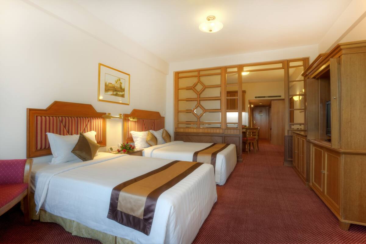 Habitación de hotel con dos camas, zona de comedor y televisor.