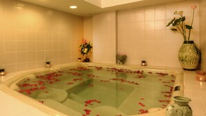 A bathtub filled with water and rose petals, surrounded by a tiled wall and a decorative vase. - Sunway Hotel Phnom Penh (Phnom Penh)