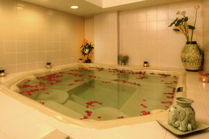 Una bañera llena de agua y pétalos de rosa, rodeada por un muro de azulejos y un jarrón decorativo.