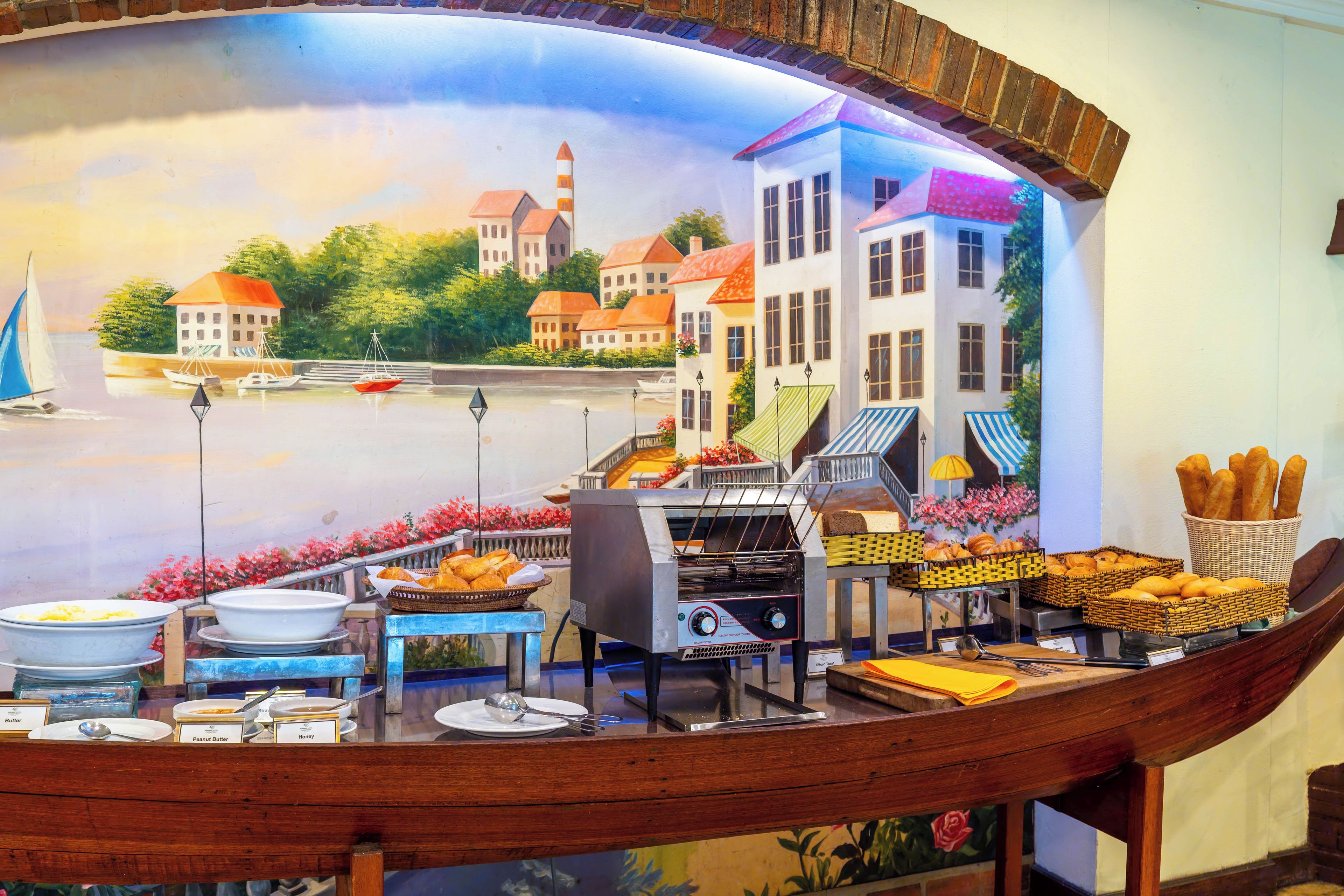 Ein Essbereich mit Blick auf eine gemalte Landschaft, einer Buffet-Anrichtung und einem bootförmigen Tisch.