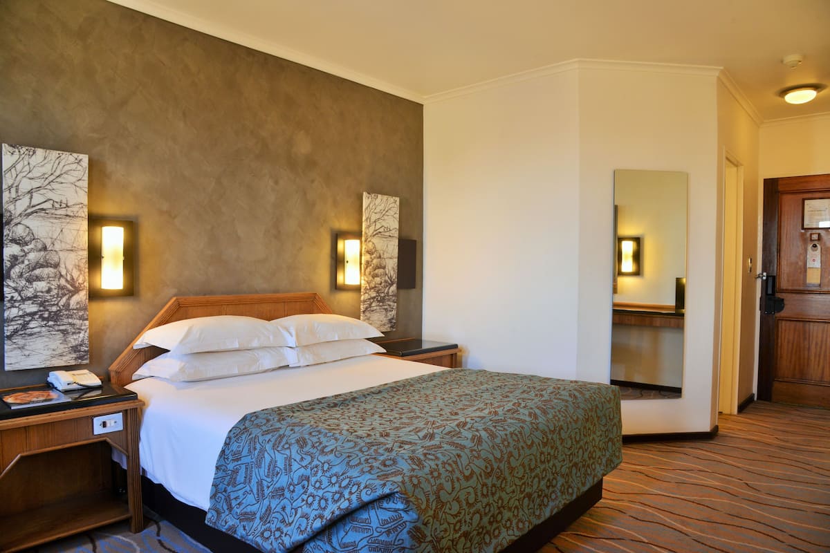 Ein Hotelzimmer mit einem großen Bett, einem Nachttisch mit Telefon, einer Wandlampe und einem Spiegel.