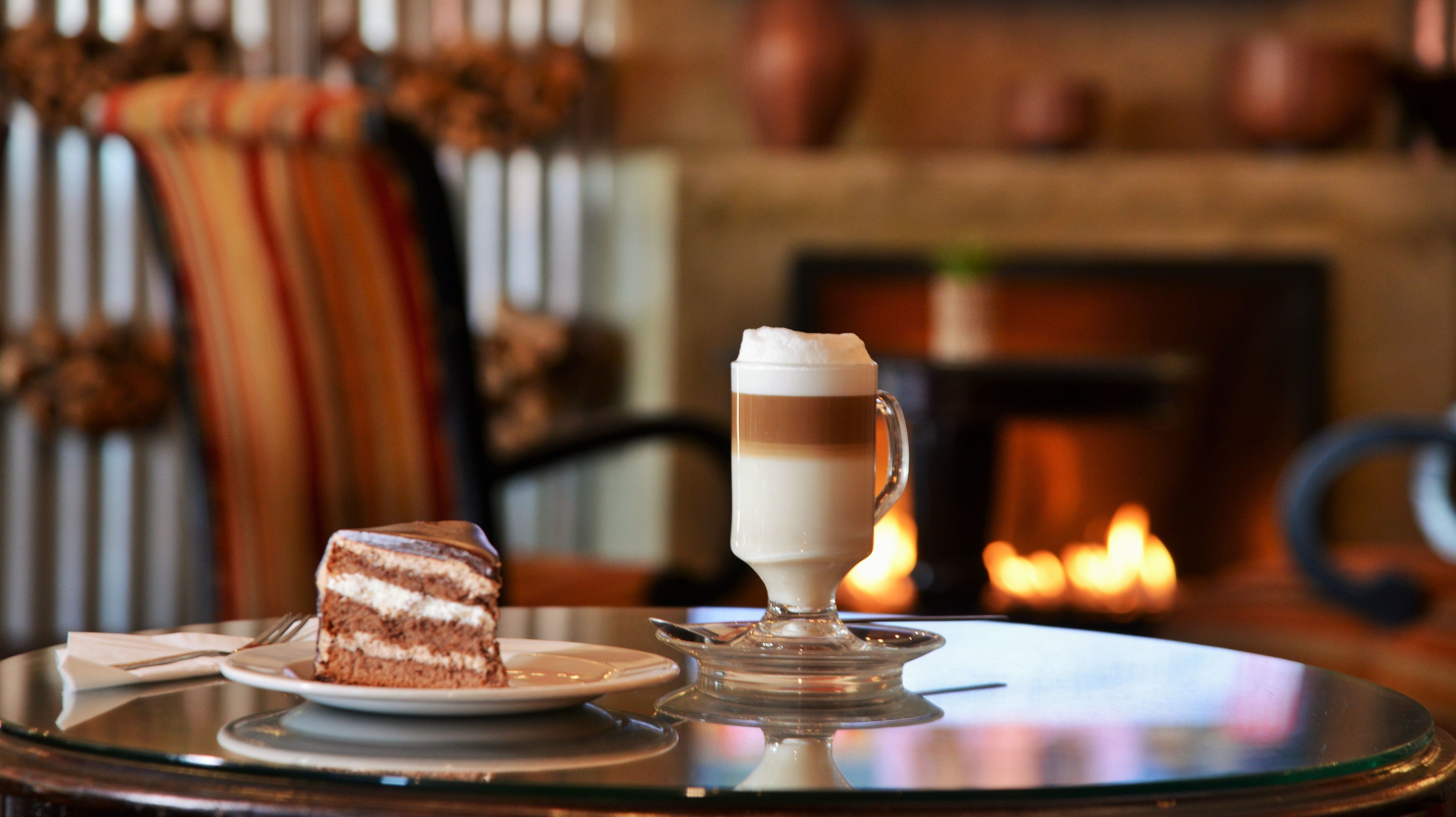 Une table en verre sur laquelle se trouvent une part de gâteau et une boisson à plusieurs couches, le tout présenté sur une assiette en verre.