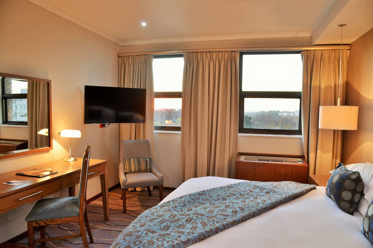 Ein Hotelzimmer mit Bett, Schreibtisch, Stuhl, Fernseher und großen Fenstern.