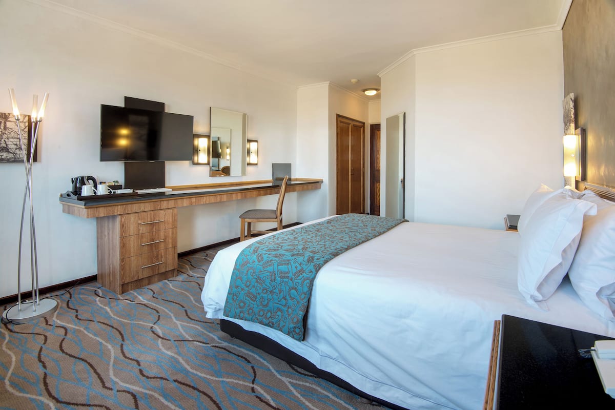Ein Hotelzimmer mit einem Bett, einem Schreibtisch mit Stuhl, einem Flachbildfernseher, einem Spiegel und einer Lampe.