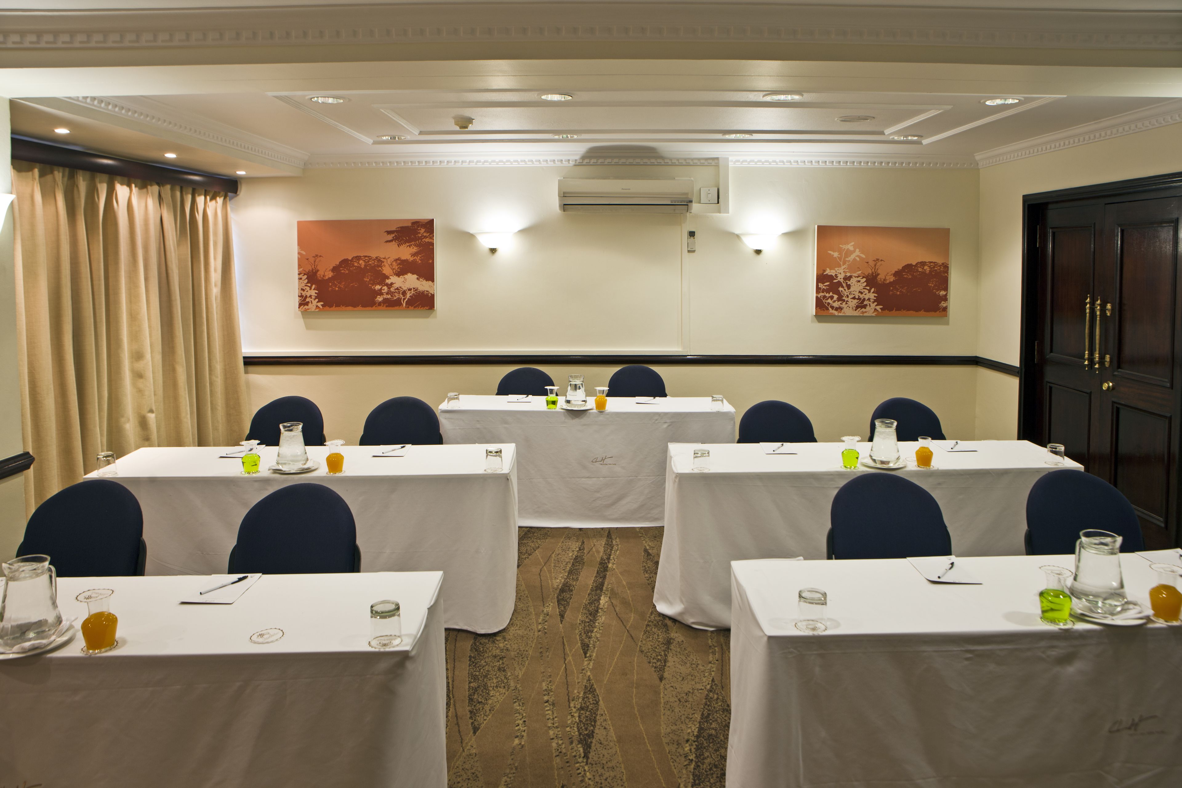 Un salón de conferencias con mesas dispuestas para una reunión, equipado con tarjetas de identificación, vasos de agua y blocs de notas.