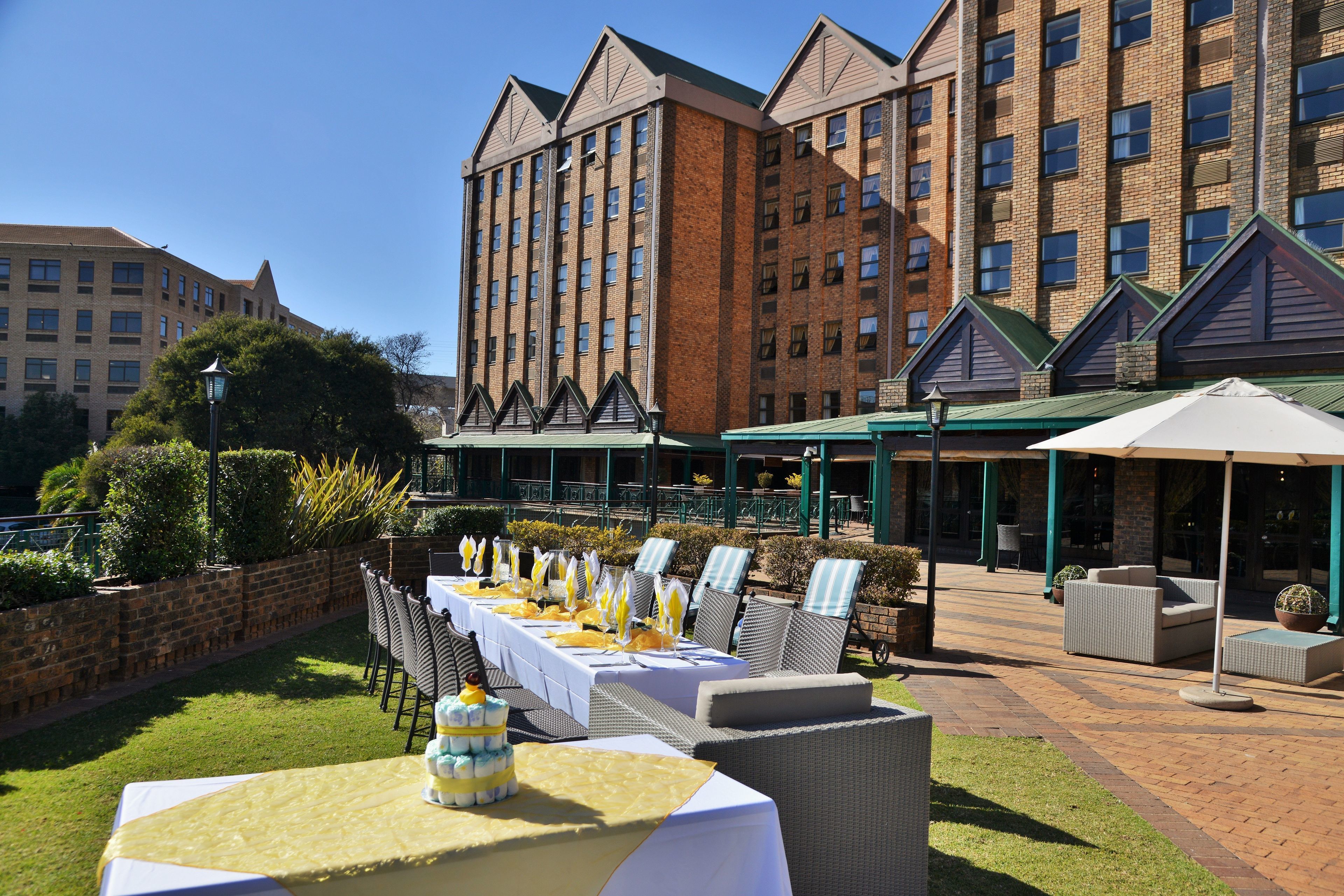 A hotel patio with outdoor seating, a long table set for dining, and a brick building in the background.