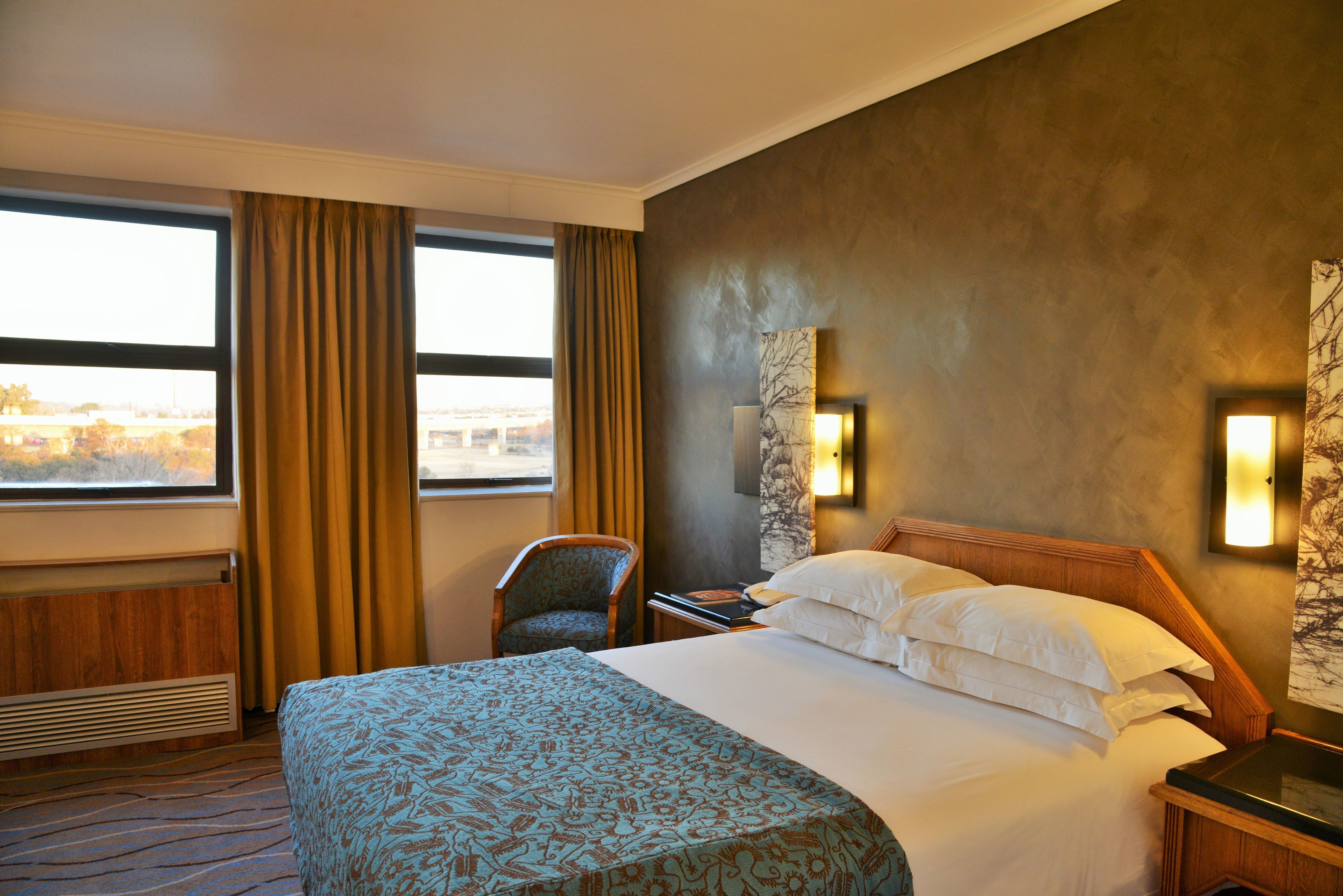 Habitación de hotel con una cama grande, una silla, una mesita de noche y vista a un puente por la ventana.