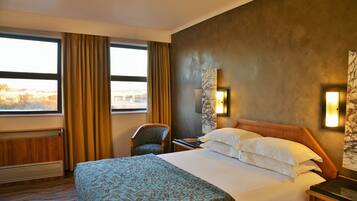 A hotel room with a large bed, a chair, a nightstand, and a view of a bridge through the window.