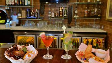 A bar area with three baskets of food, two cocktails, and a variety of bottles in the background.