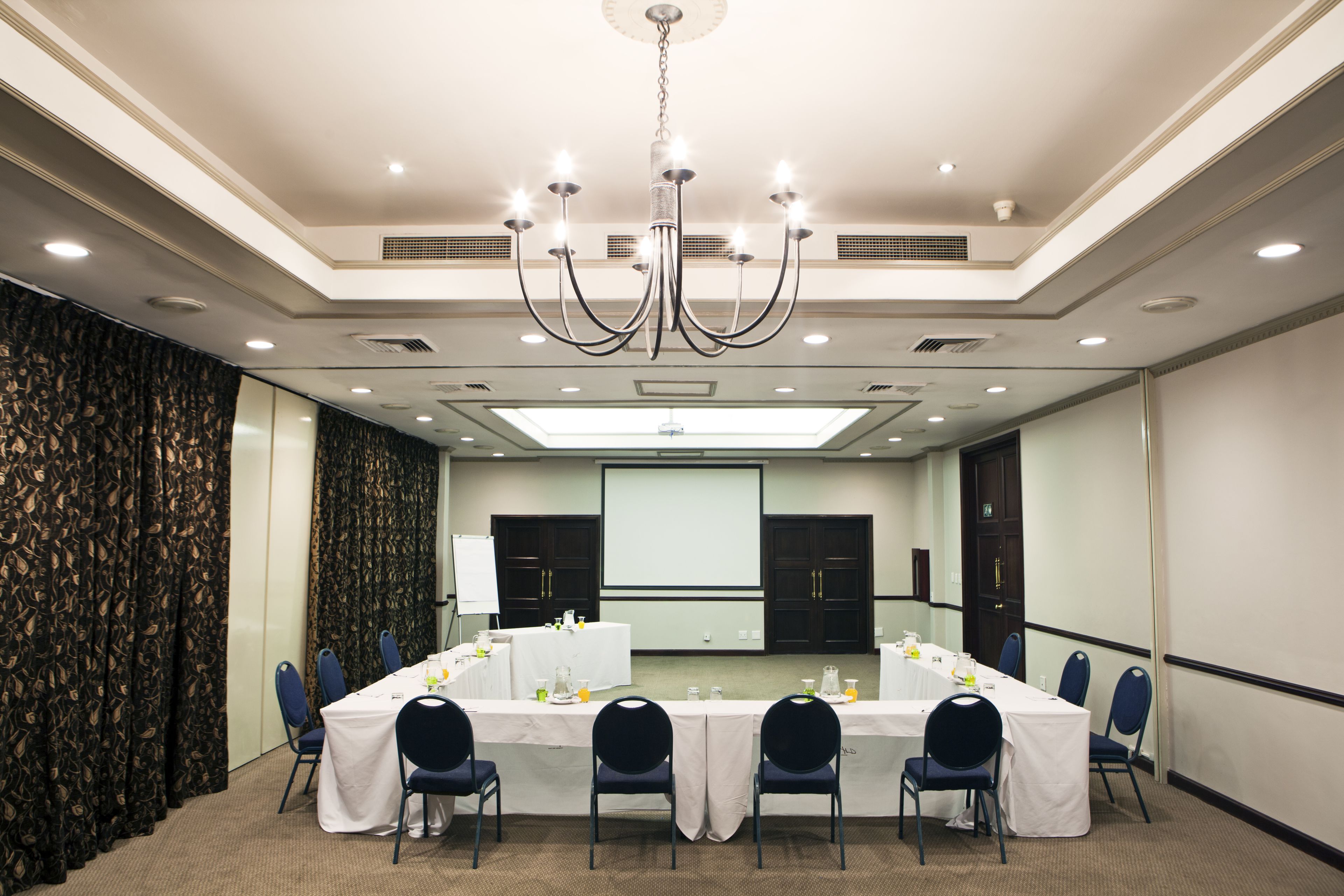 A conference room with a long table, chairs, a projector screen, and a chandelier.