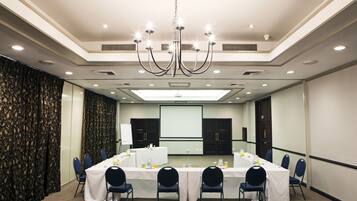 Un salón de conferencias con una larga mesa, sillas, una pantalla de proyector y una araña.