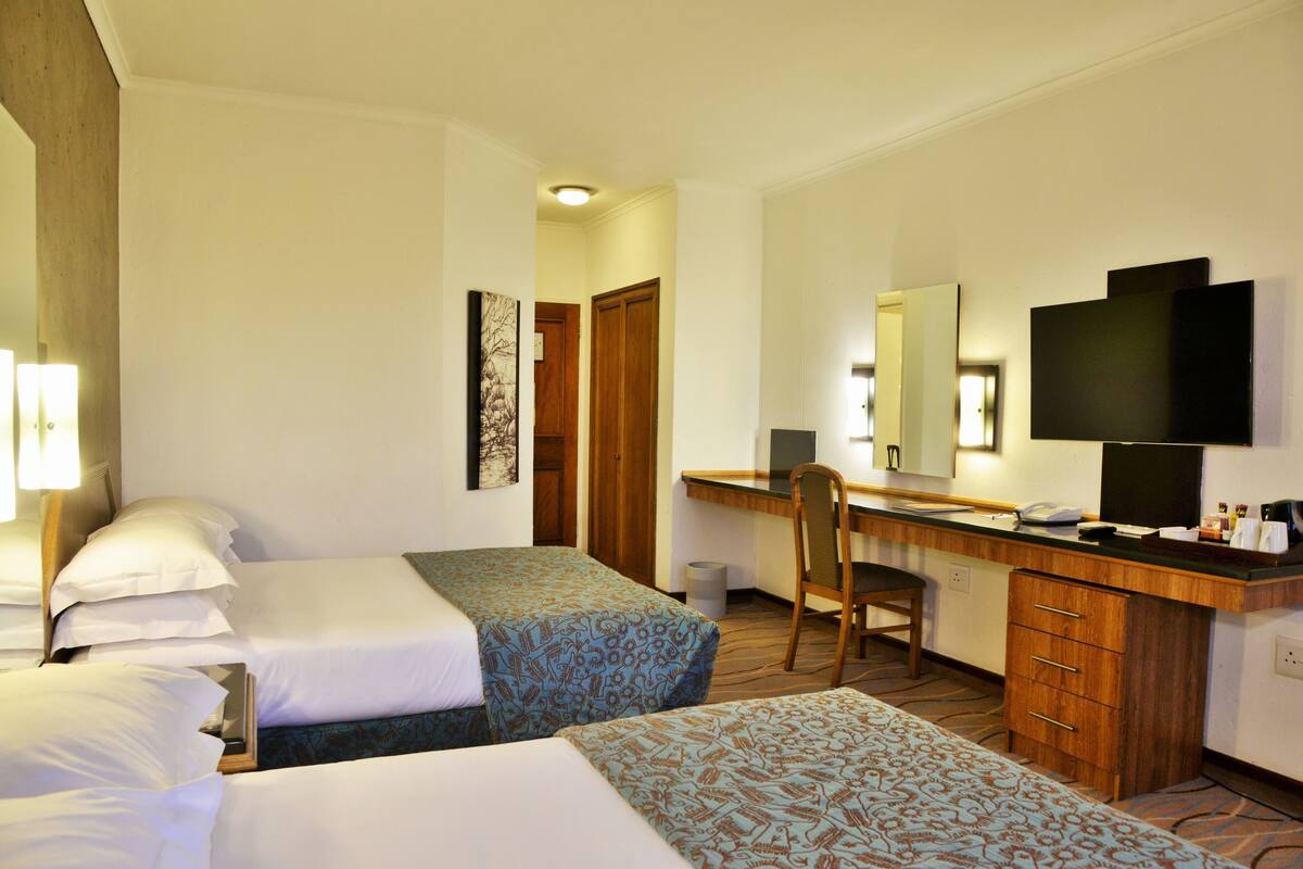 Ein Hotelzimmer mit zwei Betten, einem Schreibtisch, einem Sessel, einem Fernseher und einem Spiegel.